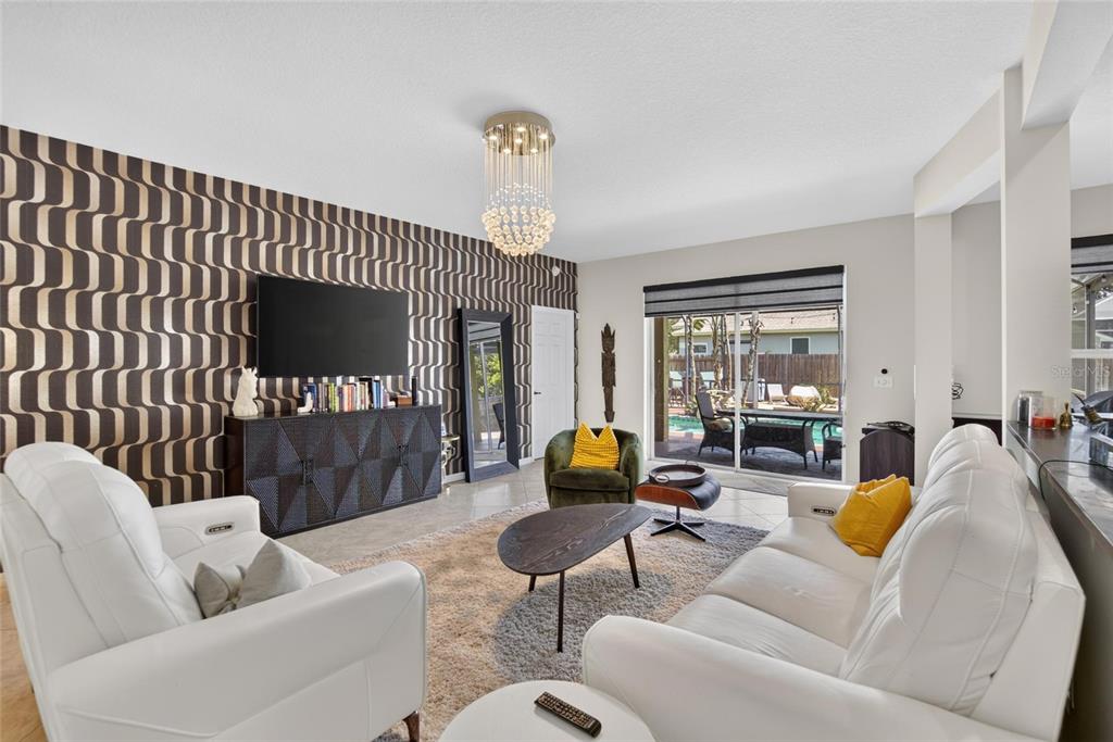 A living room features white leather sofas, a patterned accent wall, and a crystal chandelier — 12426 WINDMILL COVE DRIVE, RIVERVIEW, FL