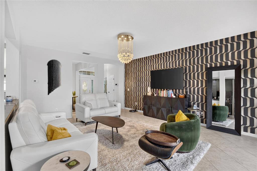 A living room features a patterned accent wall, white leather sofas, and a green armchair — 12426 WINDMILL COVE DRIVE, RIVERVIEW, FL