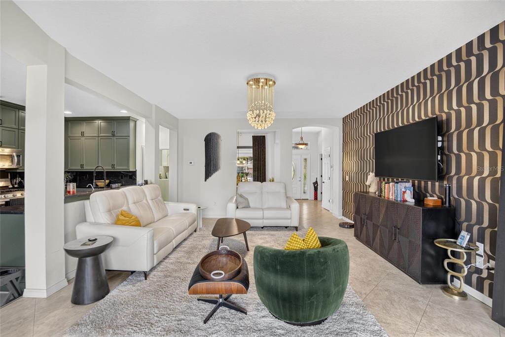 A living room features a white sofa, green velvet chair, and a patterned accent wall — 12426 WINDMILL COVE DRIVE, RIVERVIEW, FL