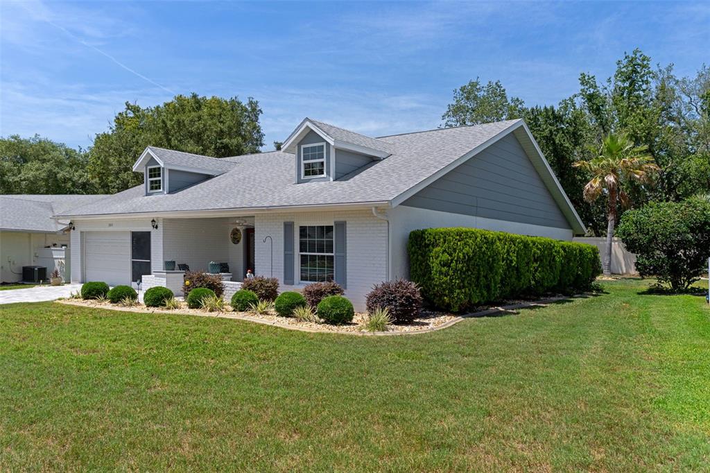 A white brick house with a gray shingled roof, dormer windows, and a manicured lawn — 2643 ROYAL RIDGE DRIVE, SPRING HILL, FL