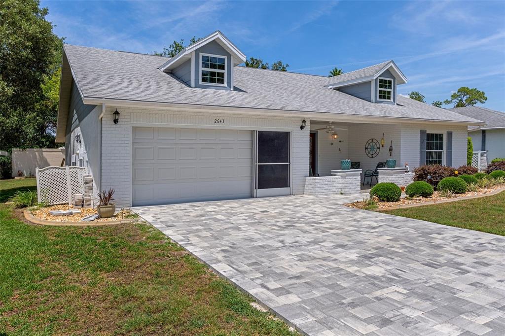 A white brick house with a paved driveway, two dormer windows, and a covered porch — 2643 ROYAL RIDGE DRIVE, SPRING HILL, FL