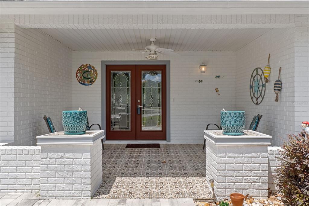 A covered front porch features white brick walls, patterned tile flooring, and double entry doors — 2643 ROYAL RIDGE DRIVE, SPRING HILL, FL