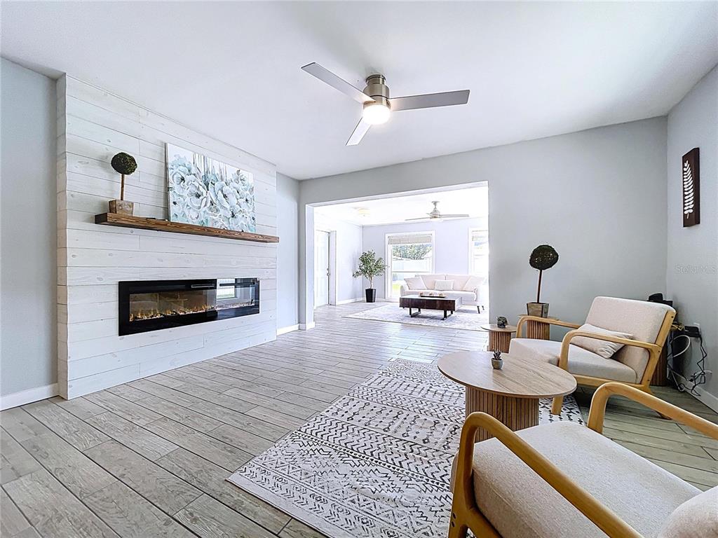 A living room features a white shiplap fireplace, light wood-look tile flooring, and two armchairs — 7960 2ND STREET N, ST PETERSBURG, FL
