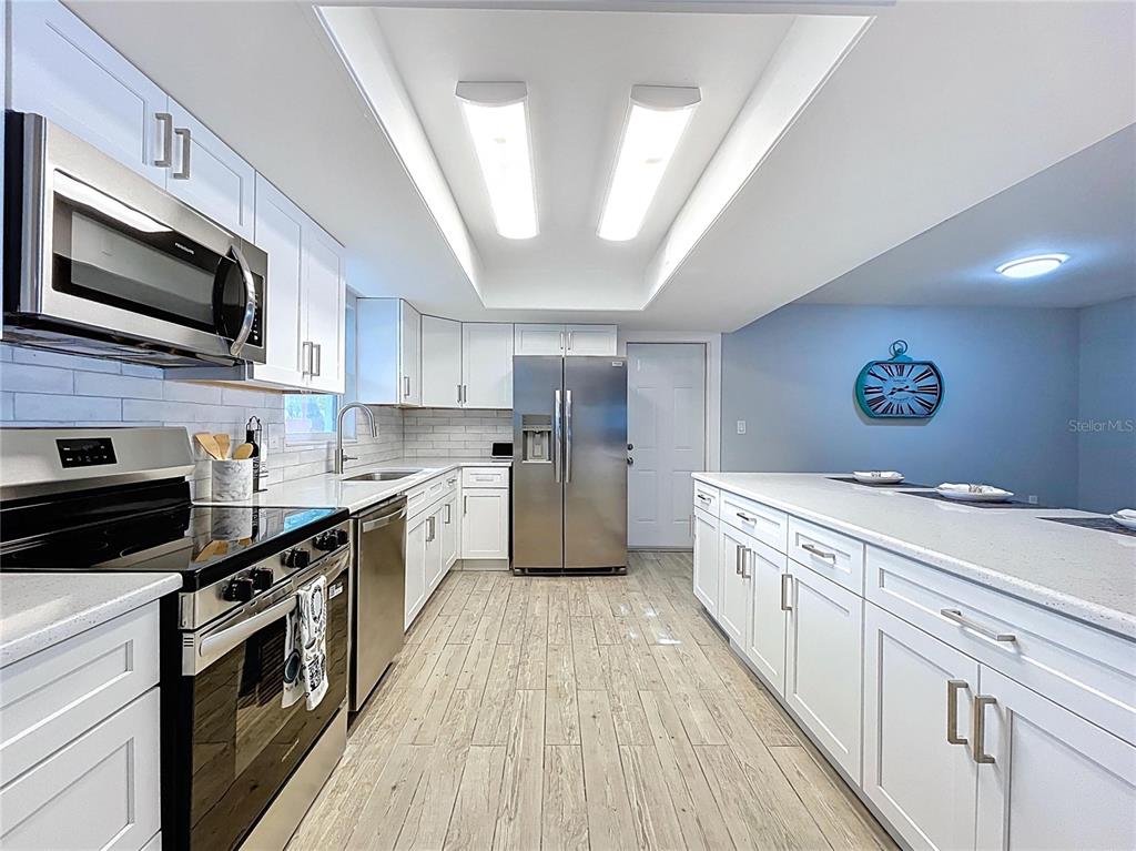 A modern kitchen features white cabinets, stainless steel appliances, and wood-look tile flooring — 7960 2ND STREET N, ST PETERSBURG, FL