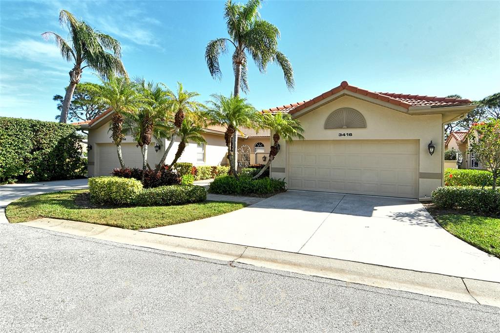 A single-story house with a beige exterior, a two-car garage, and several palm trees — 3416 W CHELMSFORD COURT UNIT 2, SARASOTA, FL