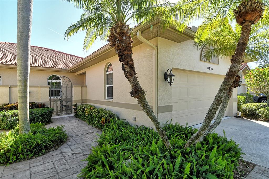 A beige stucco house exterior features a paved walkway, palm trees, and a garage — 3416 W CHELMSFORD COURT UNIT 2, SARASOTA, FL