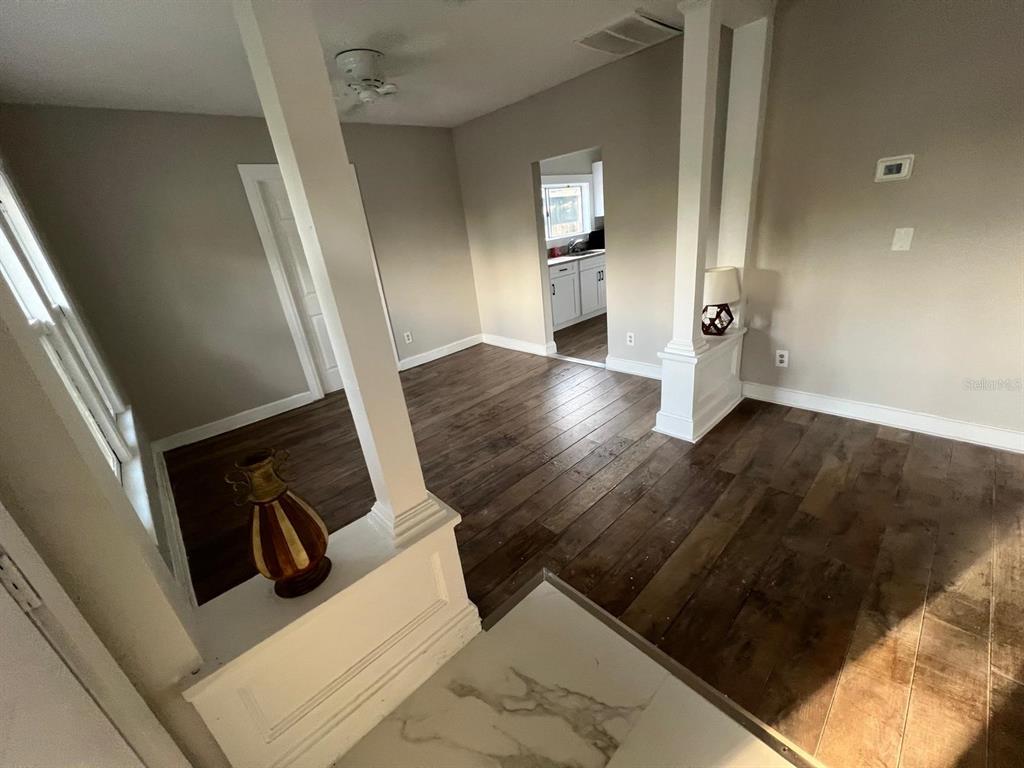 An interior view shows a living area with wood-look flooring, white columns, and a kitchen doorway — 8210 N 13TH STREET, TAMPA, FL