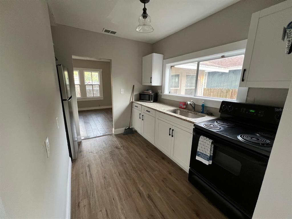 A kitchen features white cabinets, a stainless steel sink, a black stove, and wood-look flooring — 8210 N 13TH STREET, TAMPA, FL