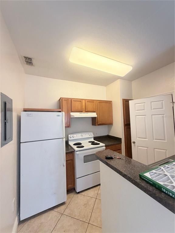 A kitchen features light-colored tile flooring, wood cabinets, a white refrigerator, and a white stove — 5525 PGA BOULEVARD SW UNIT 4625, ORLANDO, FL