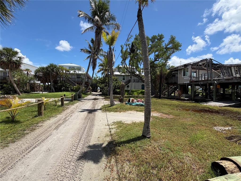 A dirt path leads between palm trees toward houses, one showing significant storm damage — 9290 LITTLE GASPARILLA ISLAND, PLACIDA, FL