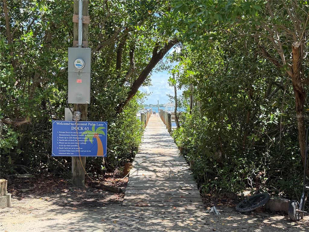 A wooden dock extends through dense trees toward the water with a posted information sign — 9290 LITTLE GASPARILLA ISLAND, PLACIDA, FL