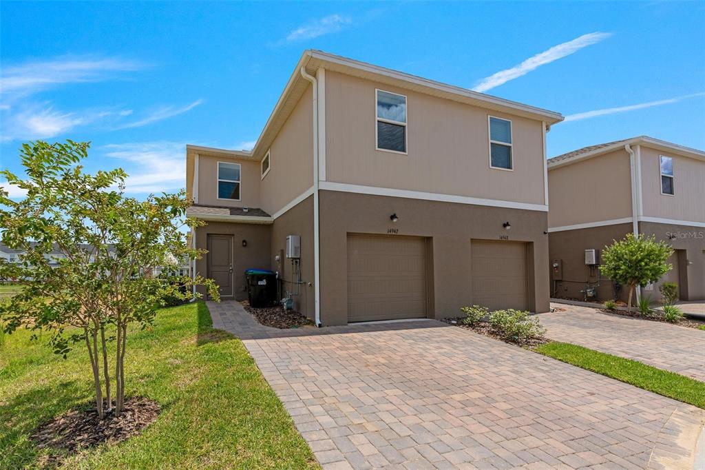 A two-story duplex with tan siding, brown stucco lower levels, and two attached garages — 14942 WINDFLOWER ALLEY, WINTER GARDEN, FL