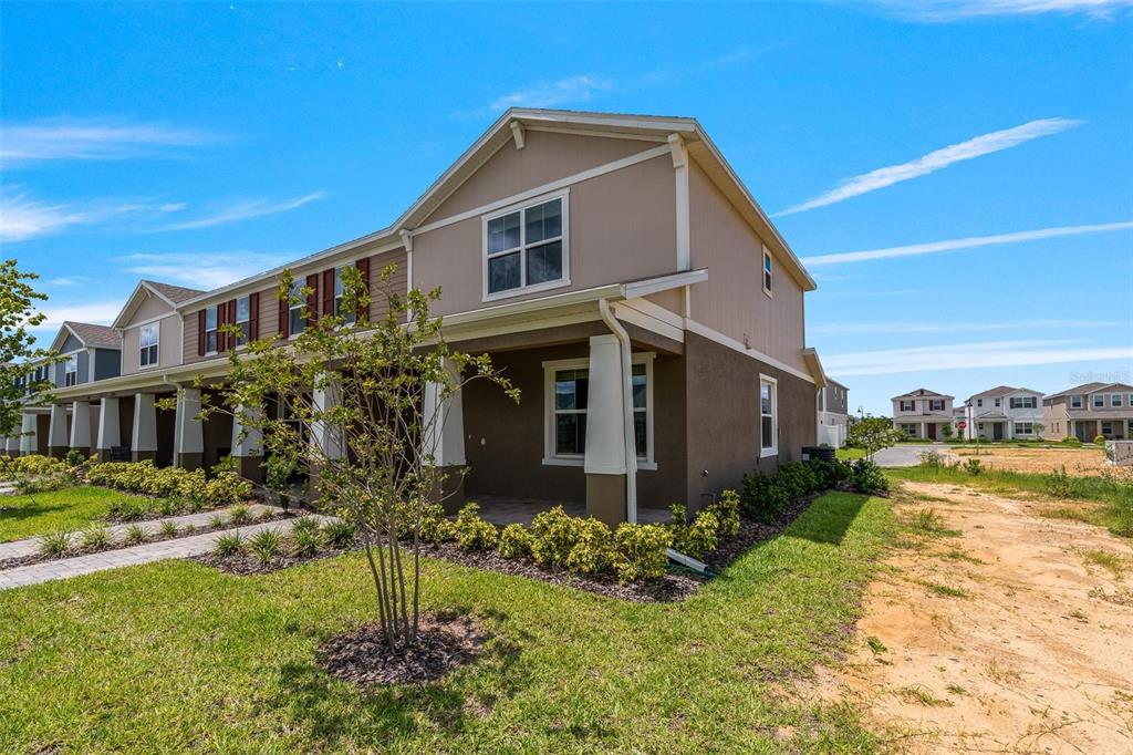 A two-story townhouse with a covered front porch and tan siding under a blue sky — 14942 WINDFLOWER ALLEY, WINTER GARDEN, FL