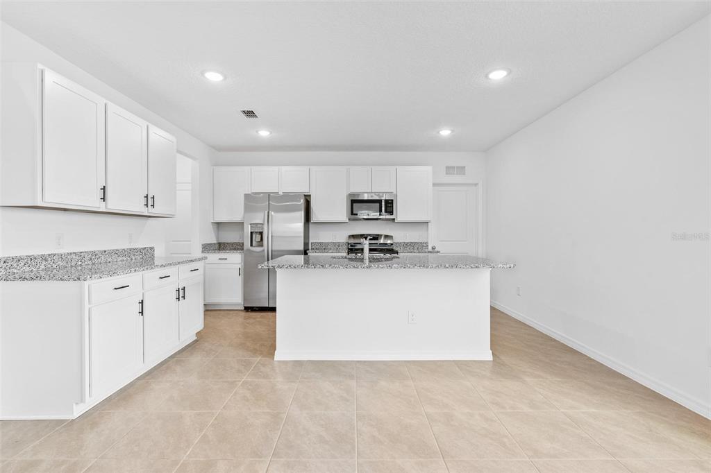 A modern kitchen features white cabinets, granite countertops, stainless steel appliances, and tile flooring — 14942 WINDFLOWER ALLEY, WINTER GARDEN, FL
