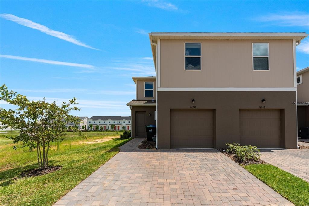 A two-story townhouse exterior features a paved driveway, two garage doors, and tan siding — 14942 WINDFLOWER ALLEY, WINTER GARDEN, FL