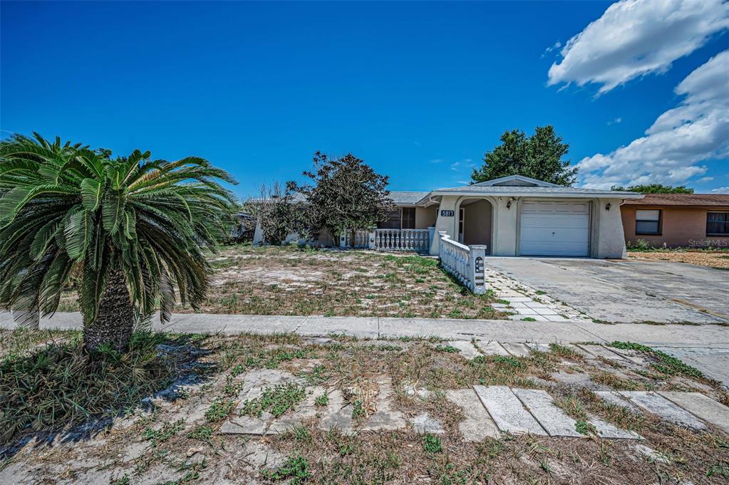 A single-story house with a white garage, a palm tree, and a sparse front yard — 5817 10TH AVENUE, NEW PORT RICHEY, FL
