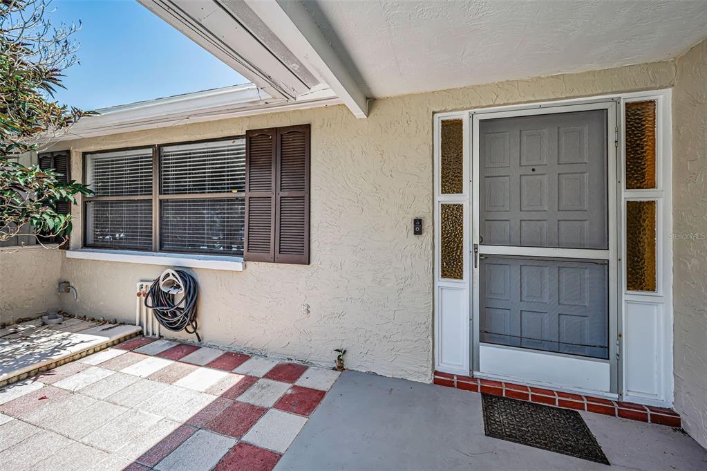 A covered entryway features a gray storm door, a checkered patio, and a window — 5817 10TH AVENUE, NEW PORT RICHEY, FL