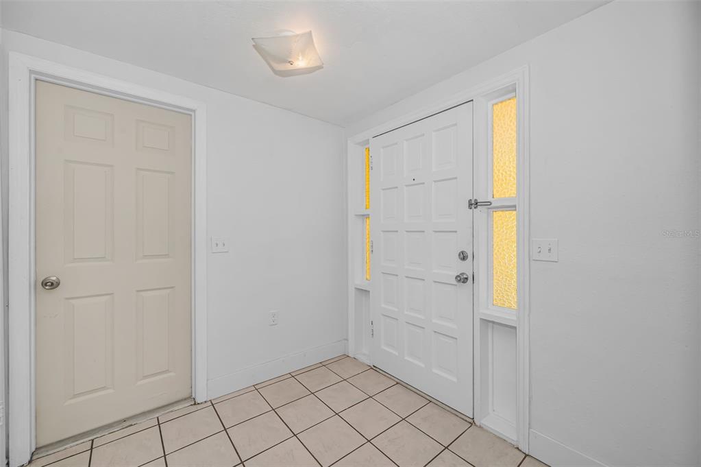An entryway features white walls, a tiled floor, a white front door, and a side door — 5817 10TH AVENUE, NEW PORT RICHEY, FL