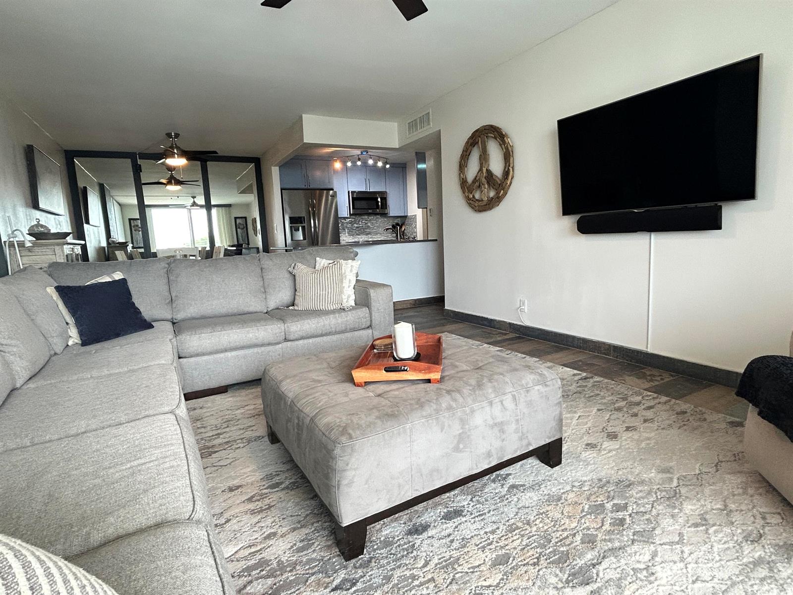 A living room with a gray sectional sofa, large ottoman, and wall-mounted television — 1009 N Ocean Boulevard N # 401, Pompano Beach FL 33062, POMPANO BEACH, FL