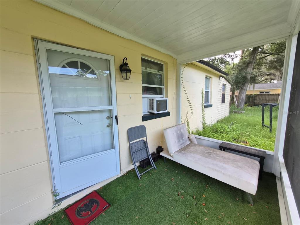 A covered porch with green turf flooring, a white door, and a lounge chair — 1012 NW 31ST AVENUE, GAINESVILLE, FL