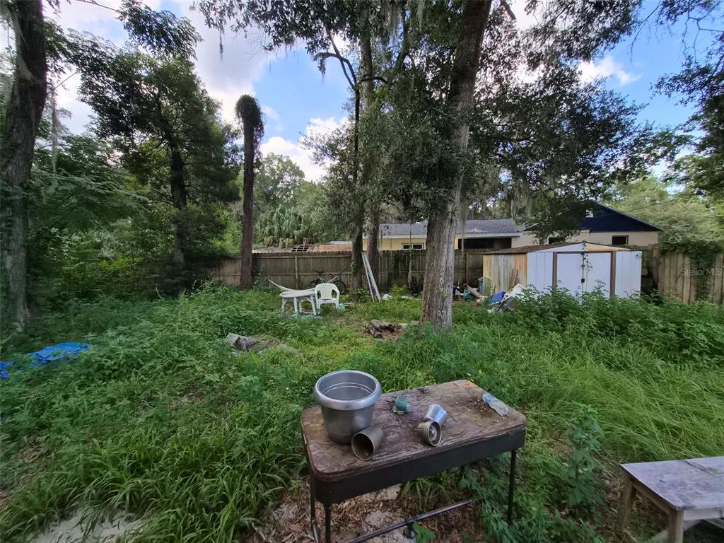 A backyard with overgrown grass, a wooden table, a white shed, and mature trees — 1012 NW 31ST AVENUE, GAINESVILLE, FL