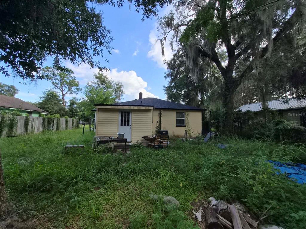 The exterior of a small, light-yellow house with a dark roof and overgrown yard — 1012 NW 31ST AVENUE, GAINESVILLE, FL