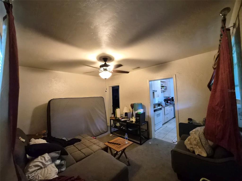 A living room with a ceiling fan, a mattress leaning against the wall, and kitchen access — 1012 NW 31ST AVENUE, GAINESVILLE, FL