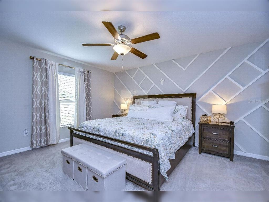 A bedroom features a bed with a patterned quilt, a tufted bench, and geometric wall molding — 1412 TAHITIAN SUNRISE DRIVE, PLANT CITY, FL