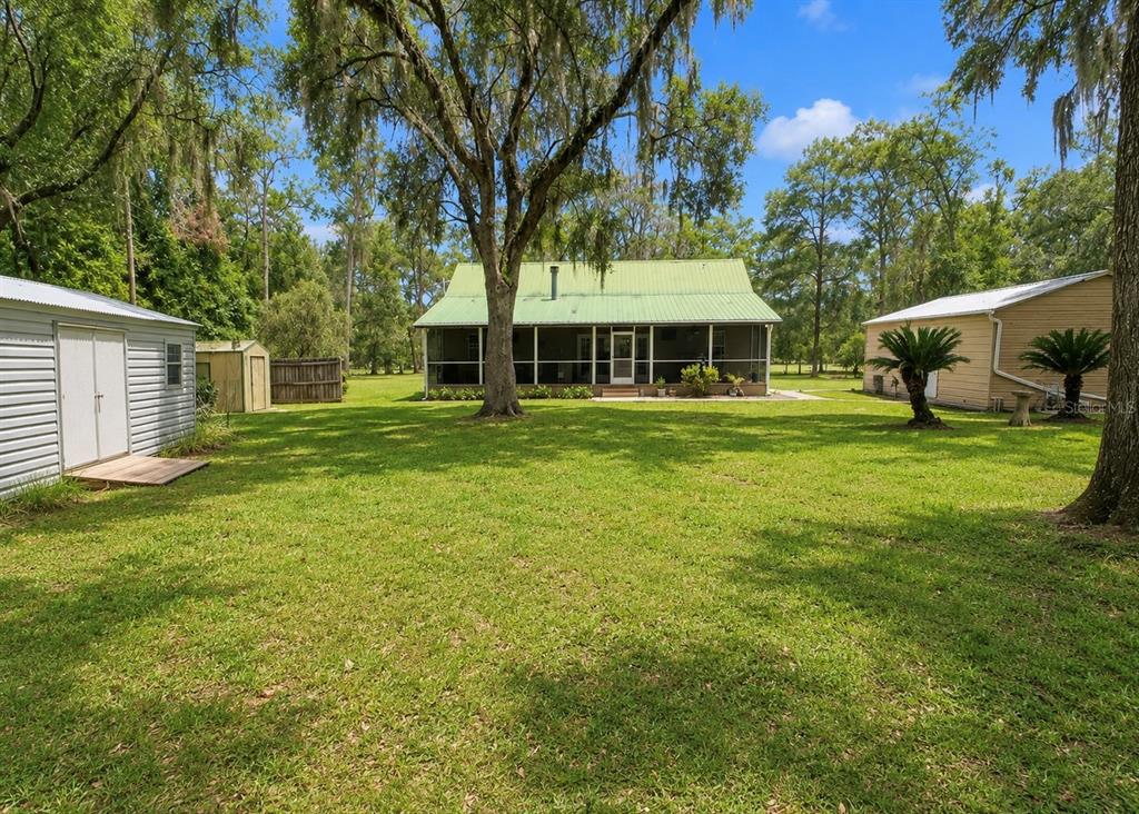 A green-roofed house with a screened porch sits on a grassy lot with two sheds — 18848 SW 60TH STREET, DUNNELLON, FL