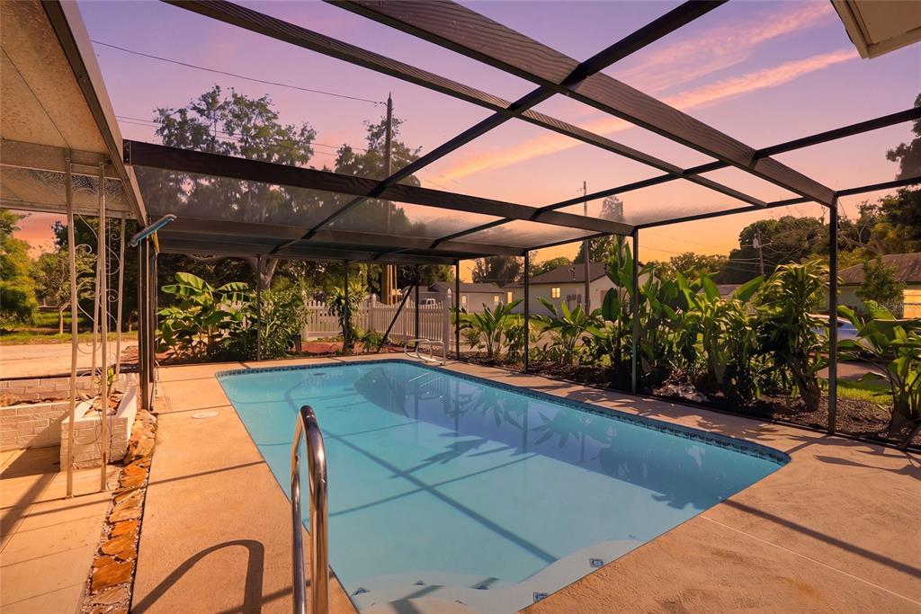 A screened-in swimming pool with a concrete deck and lush tropical landscaping at sunset — 695 41ST STREET N, ST PETERSBURG, FL