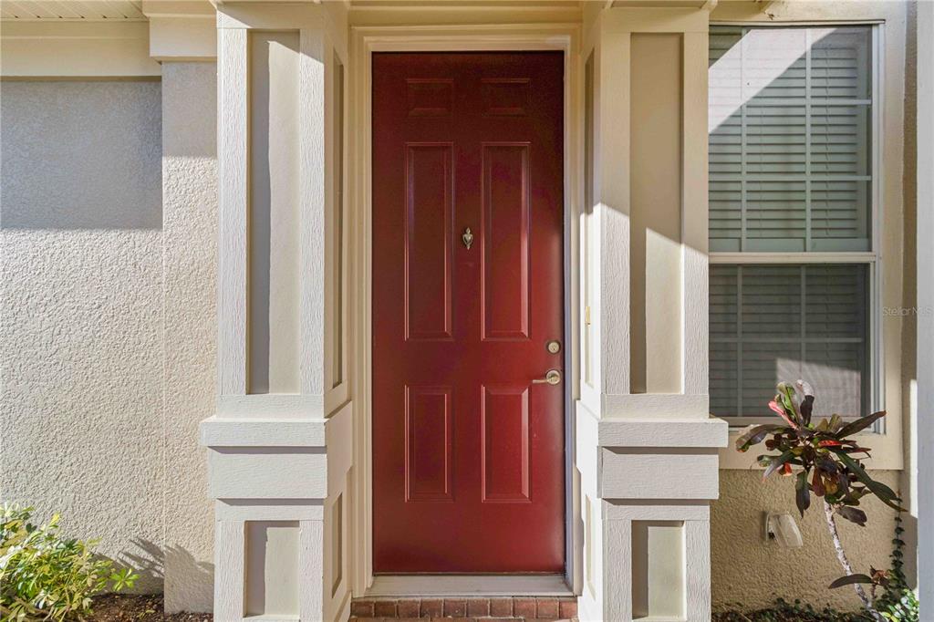 A red front door is framed by white columns and a window with shutters — 7954 TYBEE COURT UNIT 7954, UNIVERSITY PARK, FL