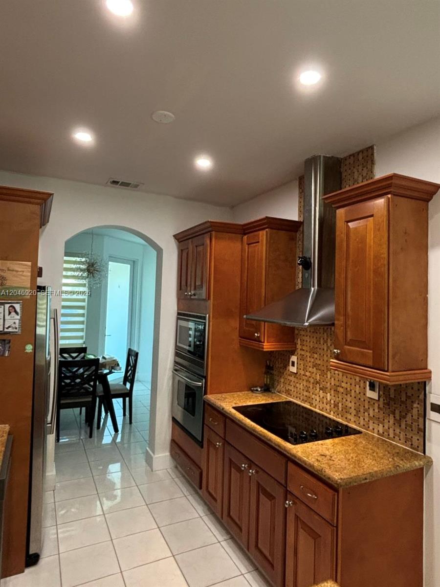 A kitchen features wood cabinets, granite countertops, a stainless steel range hood, and tile flooring — 15986 SW 71st Ter, Miami FL 33193, MIAMI, FL