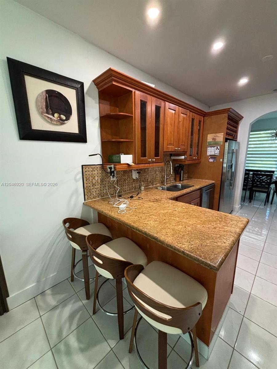 A kitchen features wooden cabinets, granite countertops, a breakfast bar with three stools, and tile flooring — 15986 SW 71st Ter, Miami FL 33193, MIAMI, FL