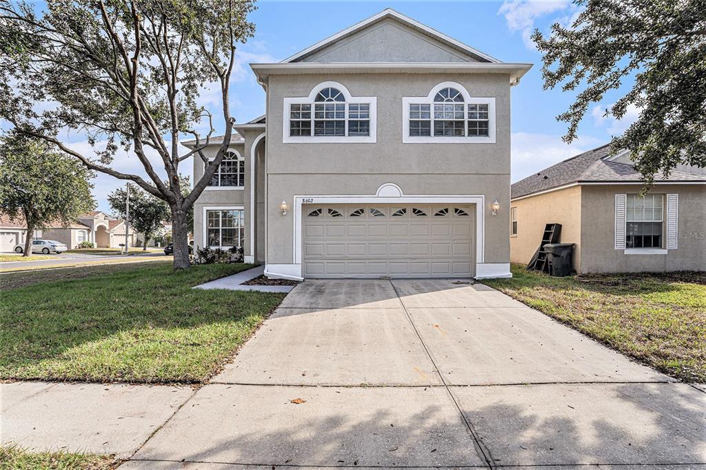 A two-story house with a beige stucco exterior, a two-car garage, and a concrete driveway — 8602 SANDY PLAINS DRIVE, RIVERVIEW, FL