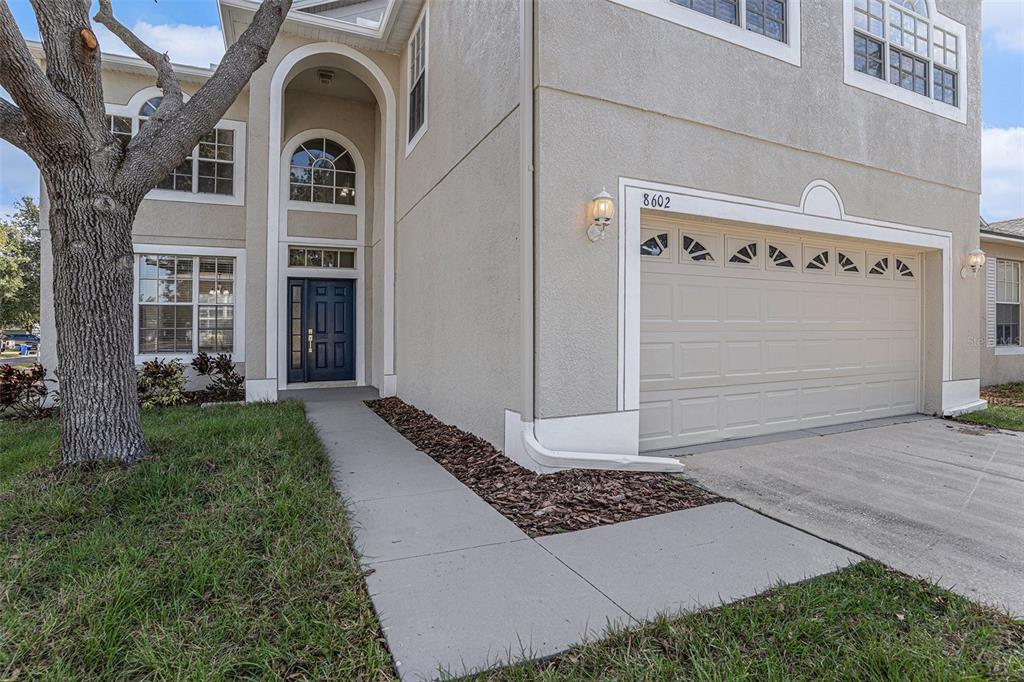 A two-story house with a beige stucco exterior, a dark blue front door, and a garage — 8602 SANDY PLAINS DRIVE, RIVERVIEW, FL