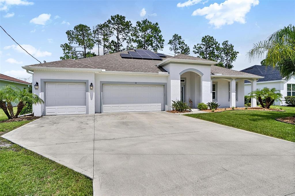A single-story house with a white stucco exterior, a three-car garage, and rooftop solar panels — 34 BUNKER HILL DRIVE, PALM COAST, FL