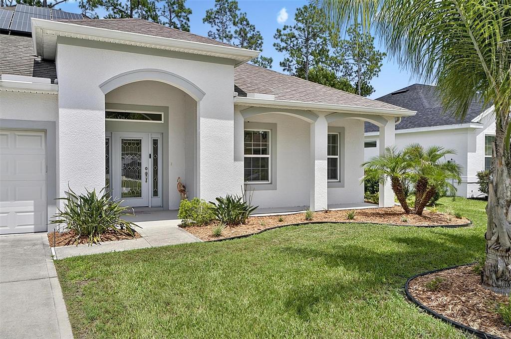 A white stucco house features a covered entryway, arched architectural details, and a front lawn — 34 BUNKER HILL DRIVE, PALM COAST, FL