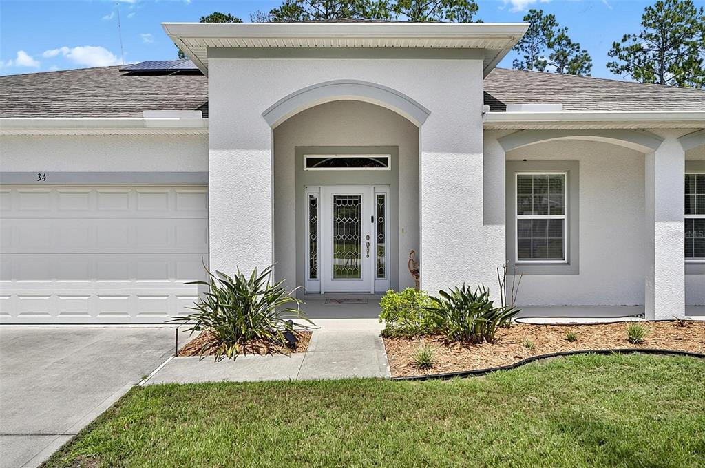 The exterior of a single-story house features a white stucco facade, arched entryway, and garage — 34 BUNKER HILL DRIVE, PALM COAST, FL