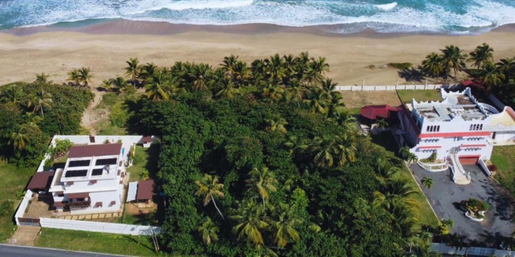 An aerial view shows two houses separated by trees along a sandy beach and ocean — Carr. 681 KM 11.7 BO. ISLOTE SEC. MELILLA, ARECIBO, PR