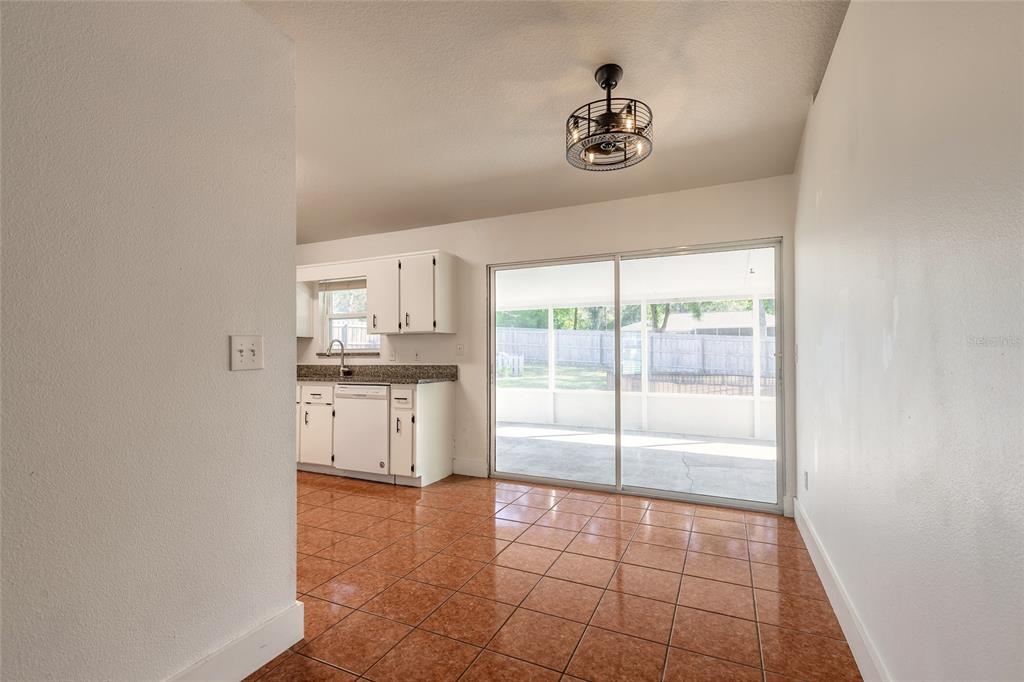 A kitchen with white cabinets and tile flooring opens to a screened-in back patio — 235 LANCASTER AVENUE, ORANGE CITY, FL