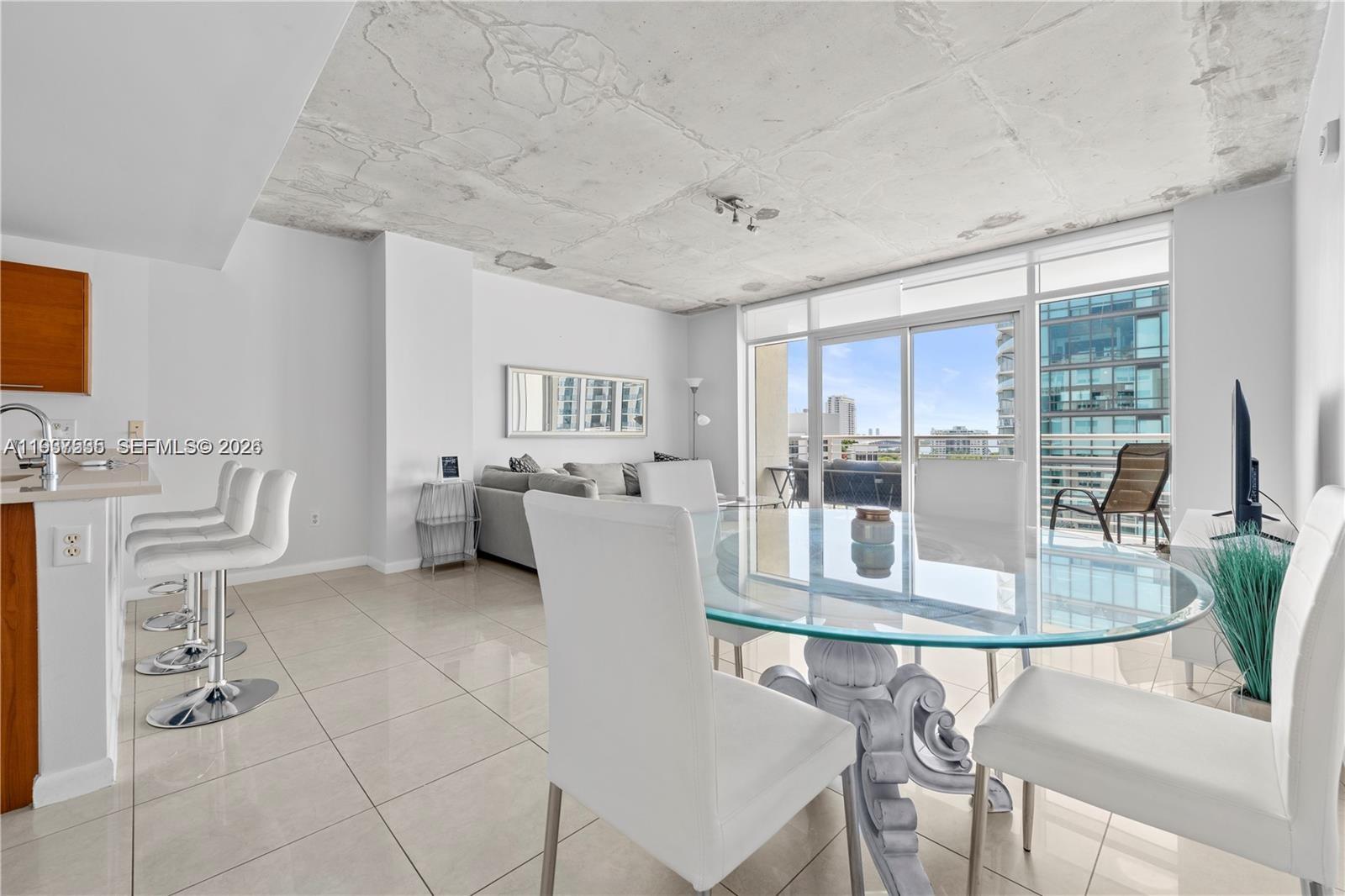 A modern open-concept living and dining area features a concrete ceiling and tile flooring — 3250 NE 1st Ave # 917, Miami FL 33137, MIAMI, FL