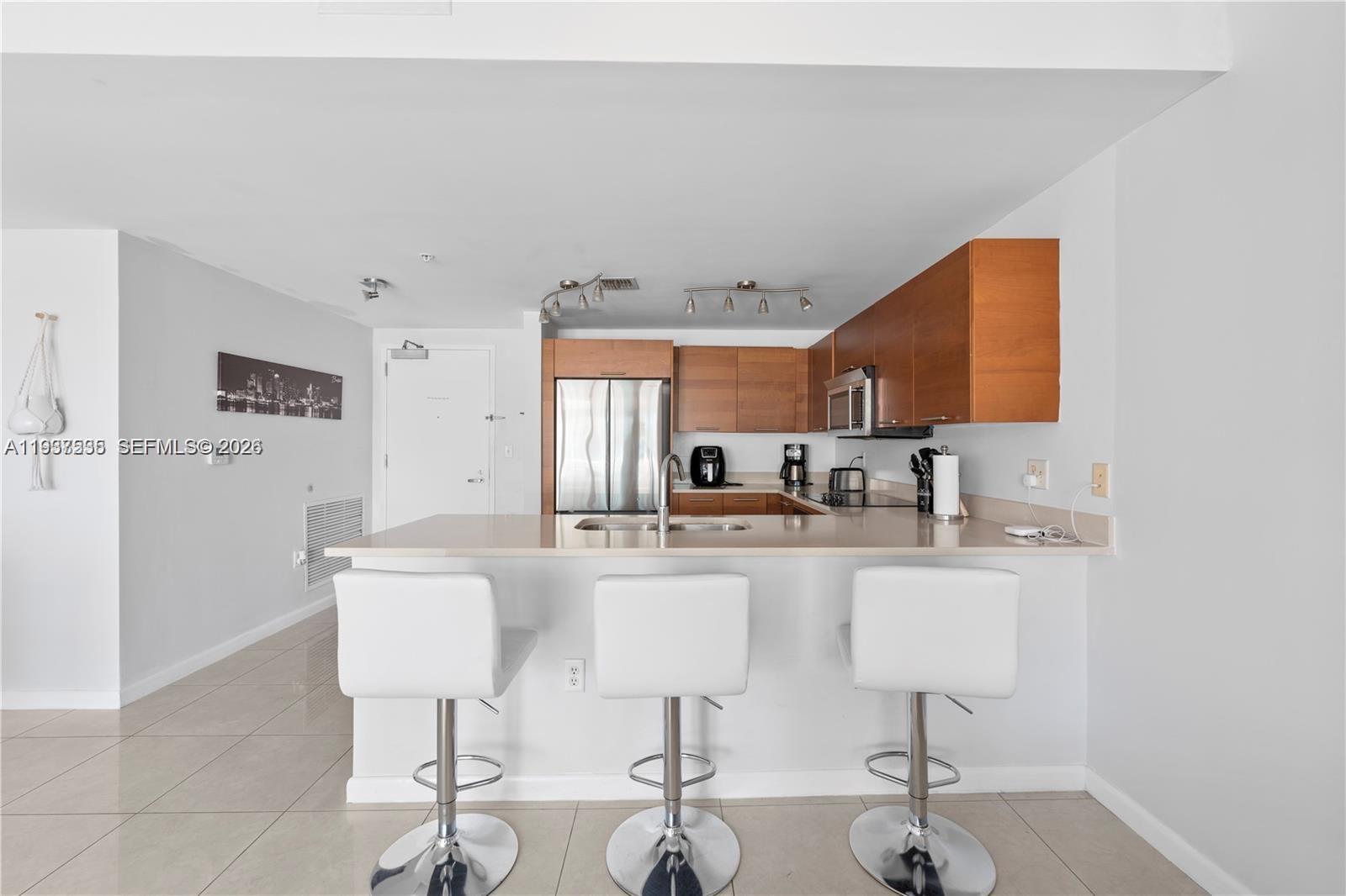 A kitchen features wood cabinets, stainless steel appliances, a breakfast bar, and three white stools — 3250 NE 1st Ave # 917, Miami FL 33137, MIAMI, FL