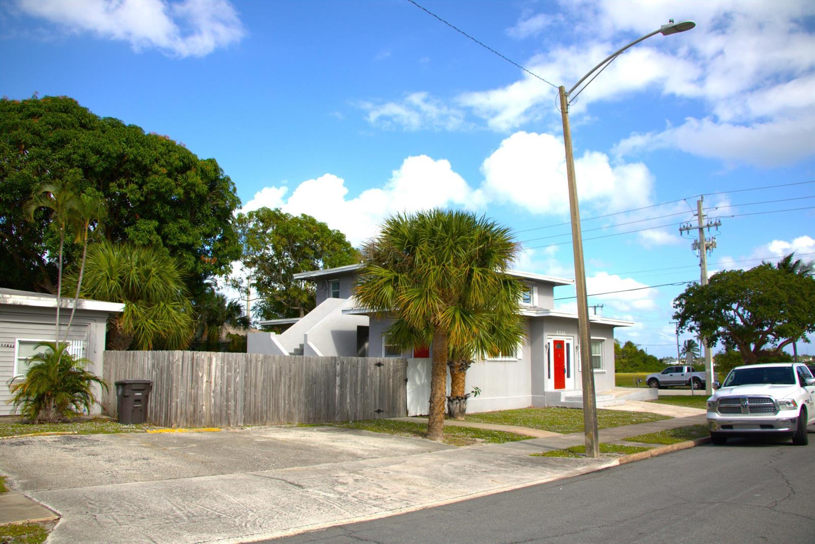 A two-story gray house with a red front door sits behind a wooden fence — 5701 N Flagler Drive, West Palm Beach FL 33407, WEST PALM BEACH, FL