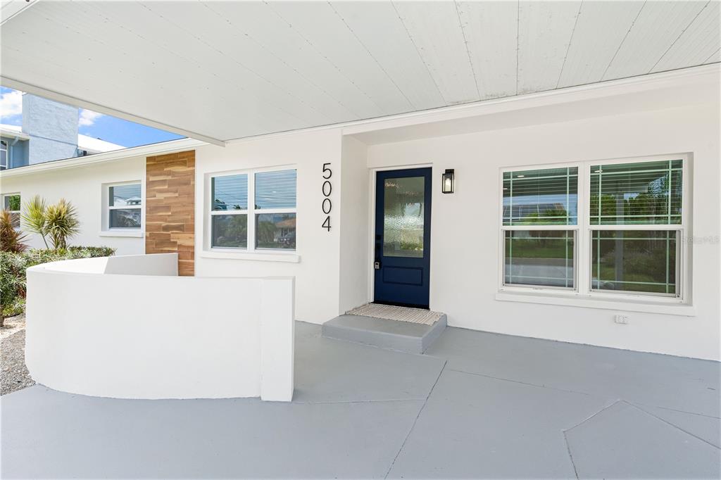 A covered porch features a blue front door, white walls, and a wood-paneled accent wall — 5004 ARLINGTON ROAD, PALMETTO, FL