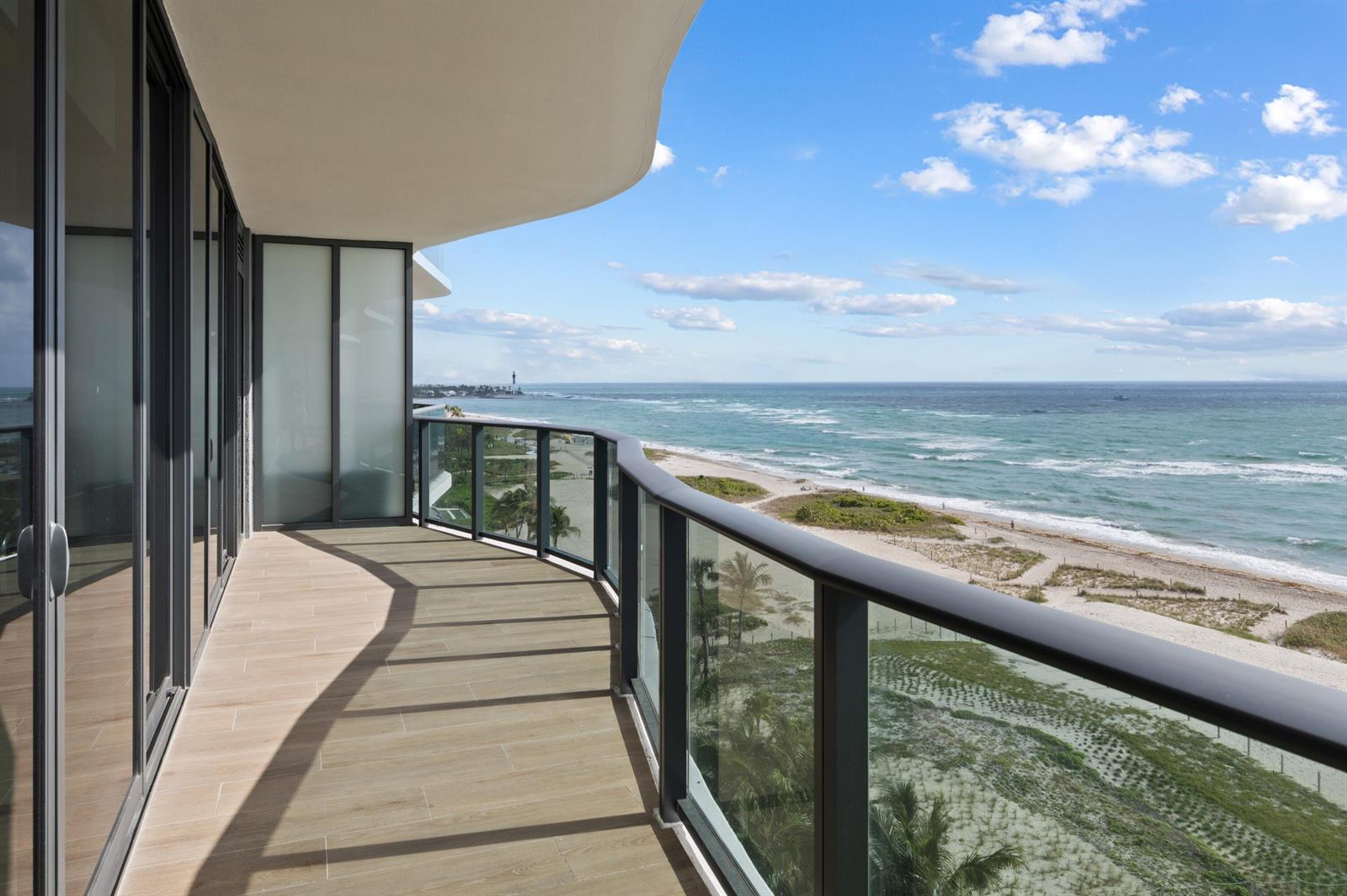 A curved balcony with wood-look tile flooring overlooks a sandy beach and the ocean — 900 N Ocean Boulevard # 802, Pompano Beach FL 33062, POMPANO BEACH, FL