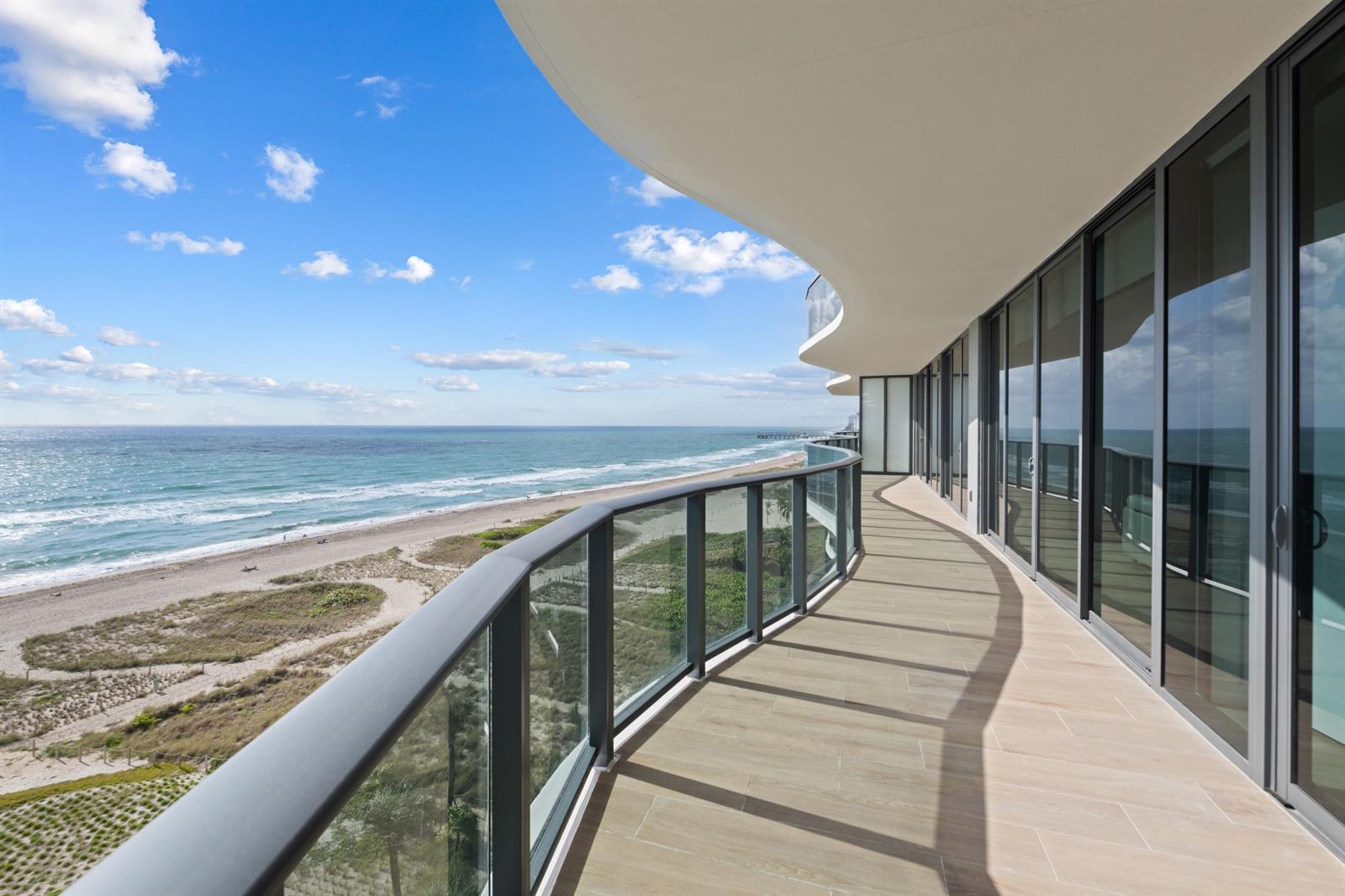 A curved balcony with glass railings overlooks a sandy beach and the ocean — 900 N Ocean Boulevard # 802, Pompano Beach FL 33062, POMPANO BEACH, FL