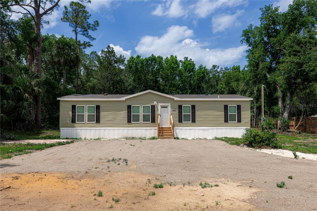 A single-story manufactured home with light green siding sits on a gravel lot — 25031 ANTLER STREET, CHRISTMAS, FL