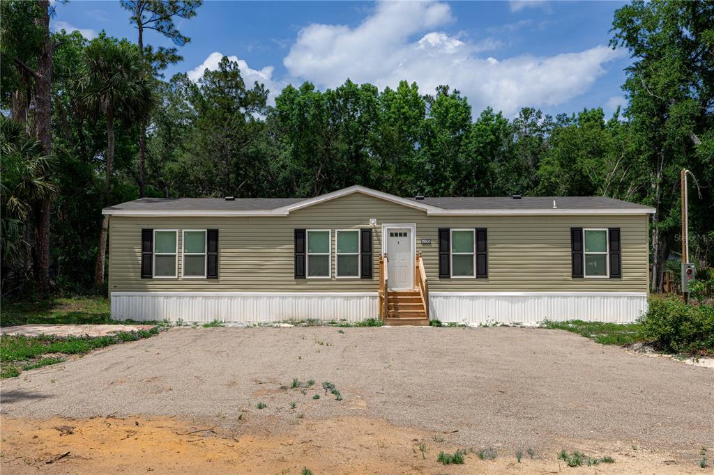 A single-story manufactured home with light green siding sits behind a large gravel driveway — 25031 ANTLER STREET, CHRISTMAS, FL