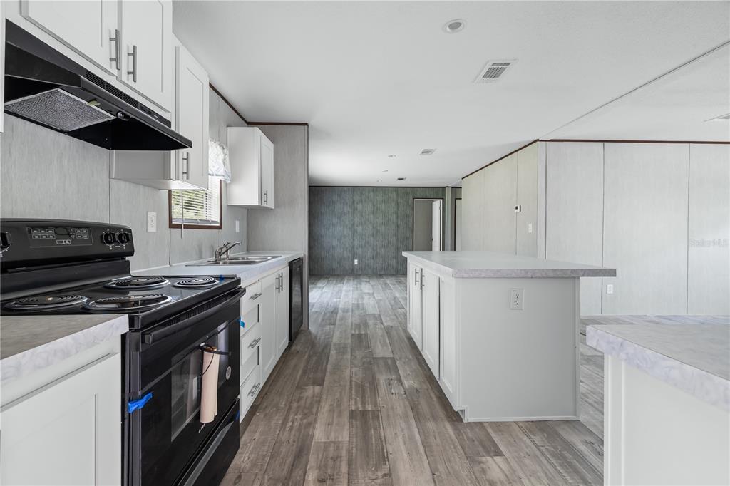 A kitchen with white cabinets, a black stove, and a central island on wood-look flooring — 25031 ANTLER STREET, CHRISTMAS, FL