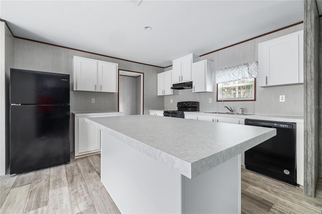 A kitchen features white cabinets, a large central island, and black appliances on wood-look flooring — 25031 ANTLER STREET, CHRISTMAS, FL